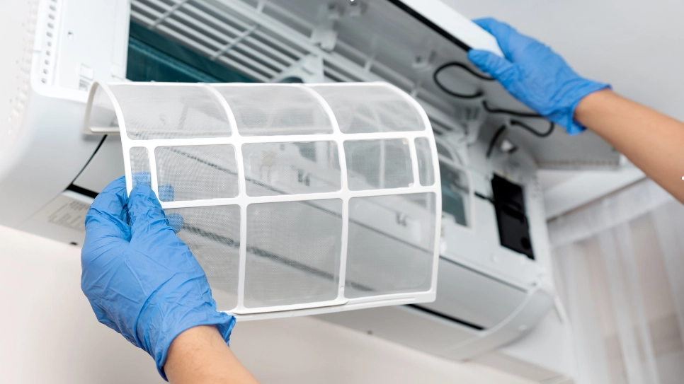 Technician wearing gloves replaces the air filter in an air conditioning unit, ensuring optimal indoor air quality and cooling efficiency.