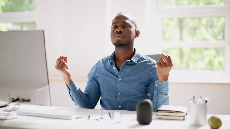 A man practicing mindfulness and relaxation techniques during a workday to combat stress and enhance productivity.