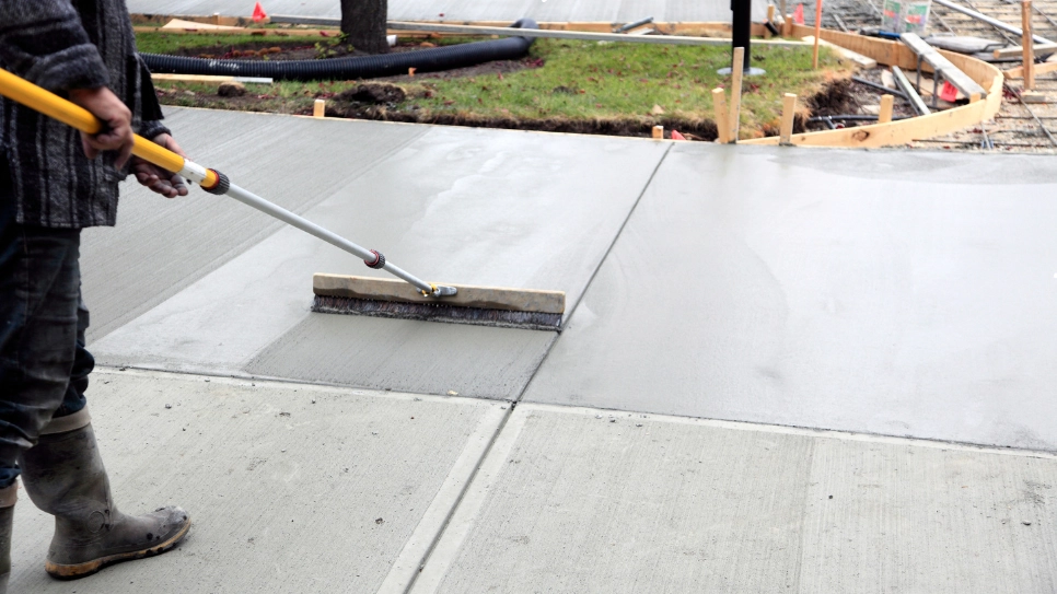 Worker using a tool to smooth a newly poured concrete driveway, ensuring a level and durable surface finish.