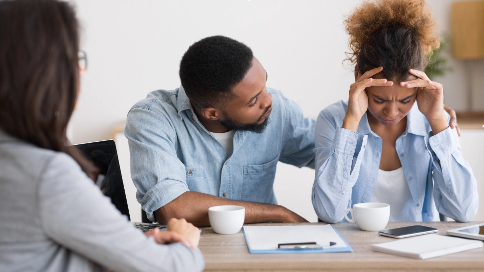 A distressed couple receiving emotional support during a counseling session, discussing relationship challenges with a professional counselor.