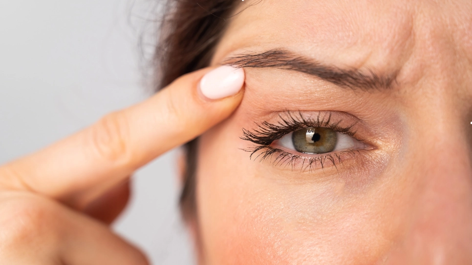 A close-up of a person gently lifting their eyelid, assessing drooping or sagging skin around the eye area.