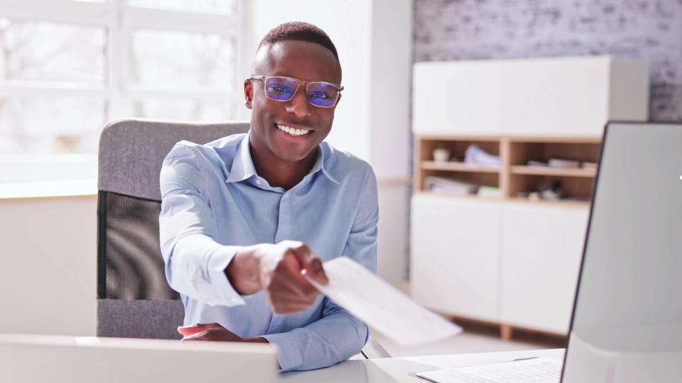 A smiling HR manager hands a document across a desk, symbolizing employee compensation or agreement.