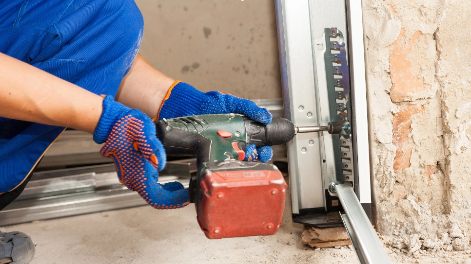 Technician using a power drill to install a garage door track, ensuring secure and precise setup for long-term functionality.