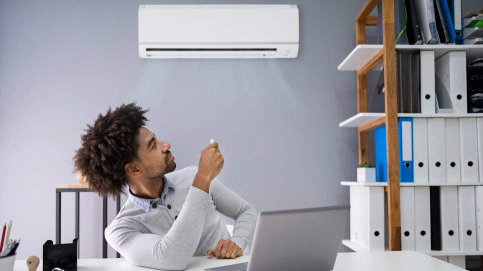 Person using a remote to control an indoor air conditioner in a modern office, ensuring a comfortable workspace.