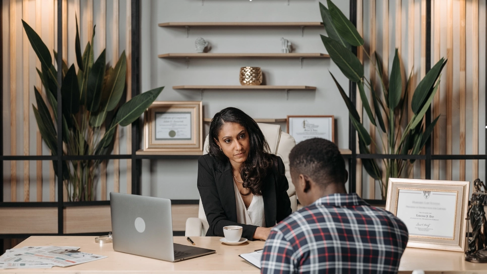 A lawyer provides legal advice to a client in an office decorated with certificates and plants, emphasizing a professional consultation setting.