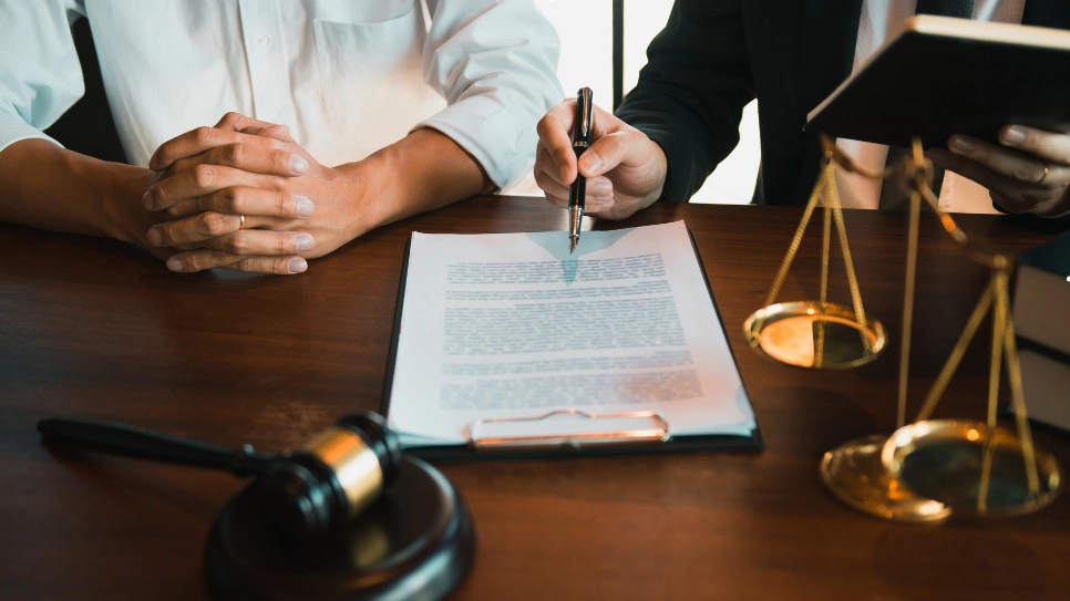 A lawyer discusses a legal document with a client at a desk, featuring scales of justice and a gavel, symbolizing legal advice and consultation.