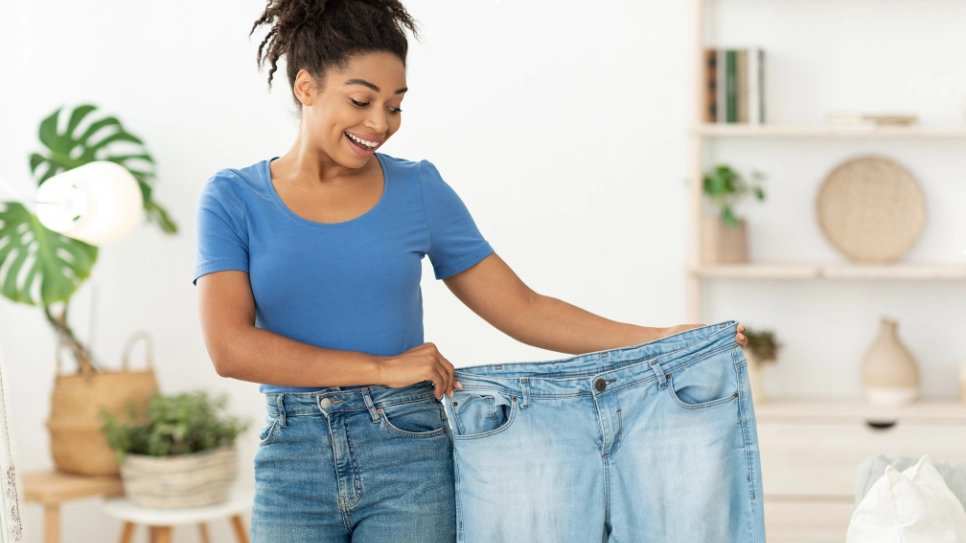 Woman holding oversized jeans, highlighting significant weight loss and body transformation achieved through liposuction.