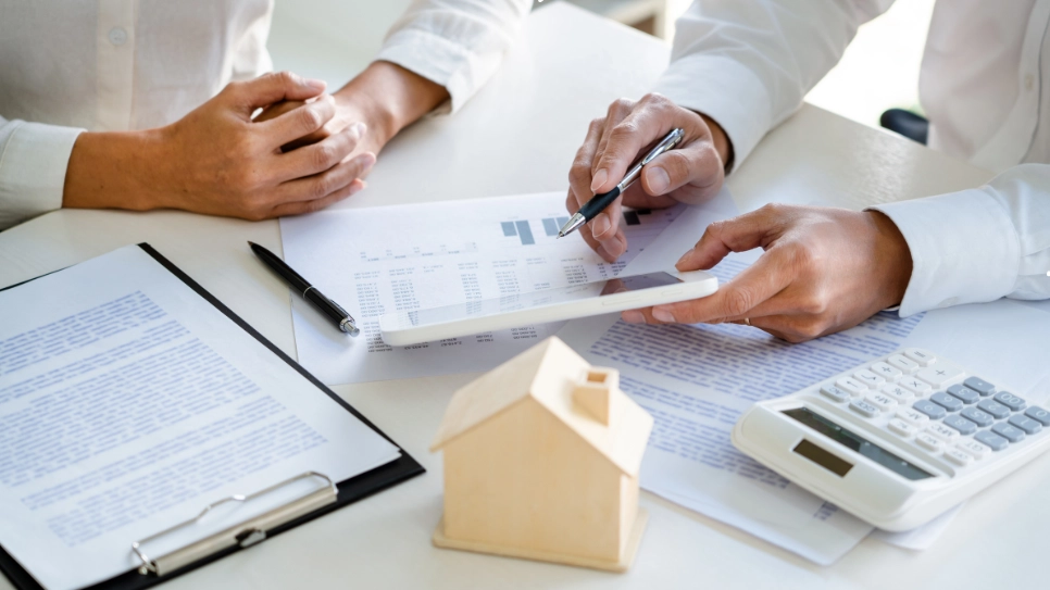 Real estate agents analyzing financial documents and statistics for real estate investment planning with a small house model on the desk.