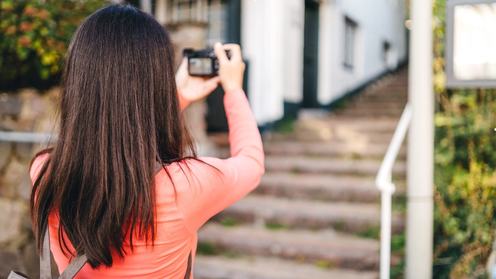 Woman photographing the exterior of a property, focusing on real estate photography for property listing visuals.