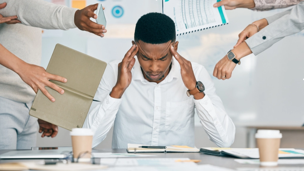 A stressed office worker surrounded by colleagues presenting tasks and documents, illustrating workplace burnout and the need for stress management solutions.