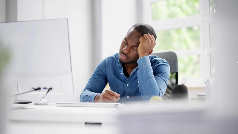 A man overwhelmed at his desk, showcasing common symptoms of stress and fatigue in a work environment.