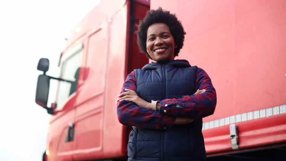 Smiling female truck driver standing confidently in front of a red truck.