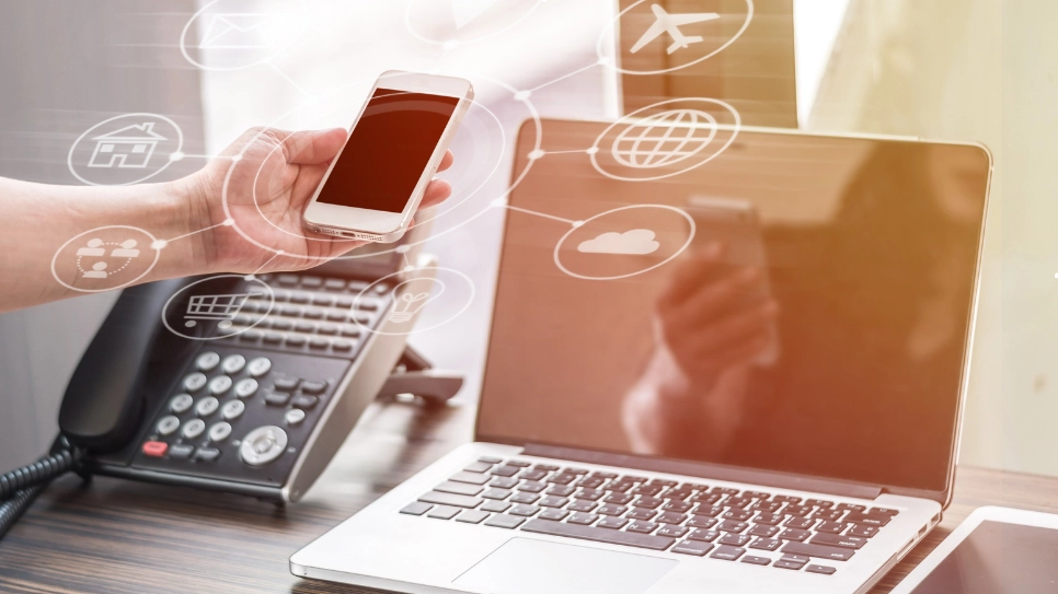 A desk setup with a landline phone, laptop, and smartphone illustrating cloud-based VOIP connectivity.