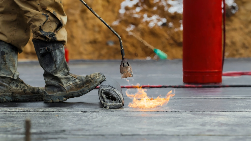 Worker in boots waterpoofing flat roof with a torch.