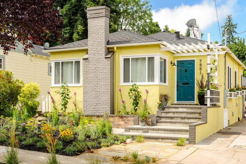 A house in the suburbs with a bright yellow exterior and a grey chimney and roof.