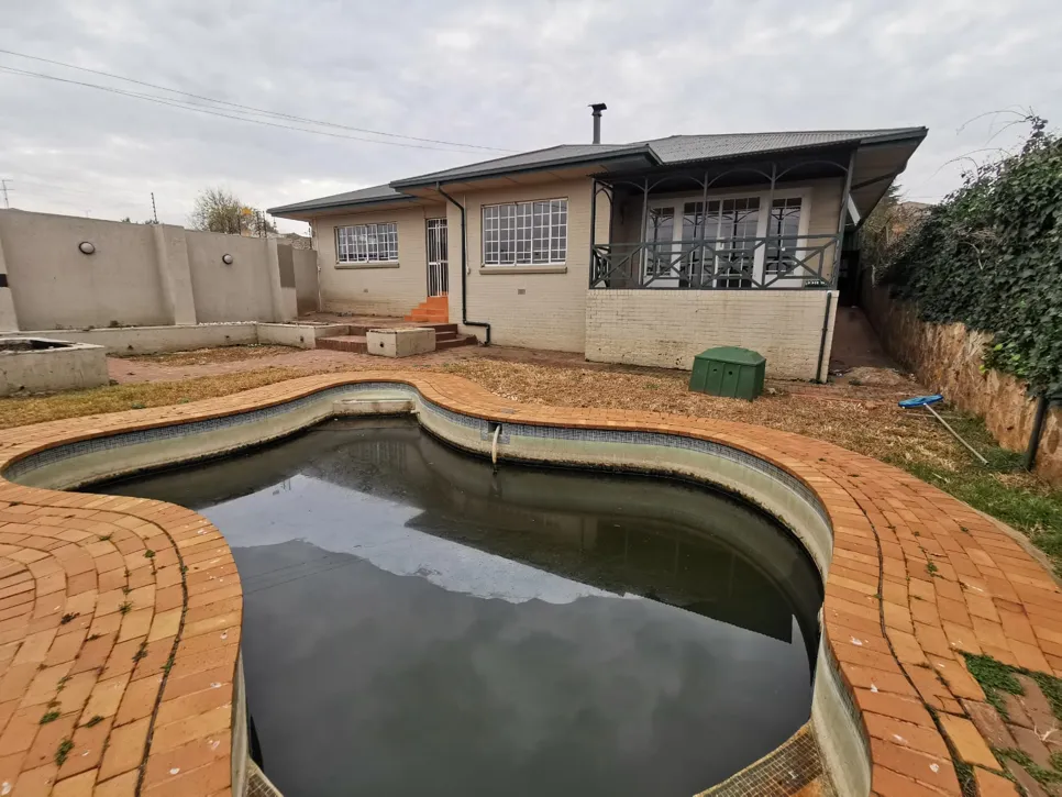 Neglected backyard pool with murky water A backyard pool with murky water and surrounding brick patio, indicating neglect and potential maintenance needs.